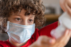 child wearing mask putting on hand sanitiser