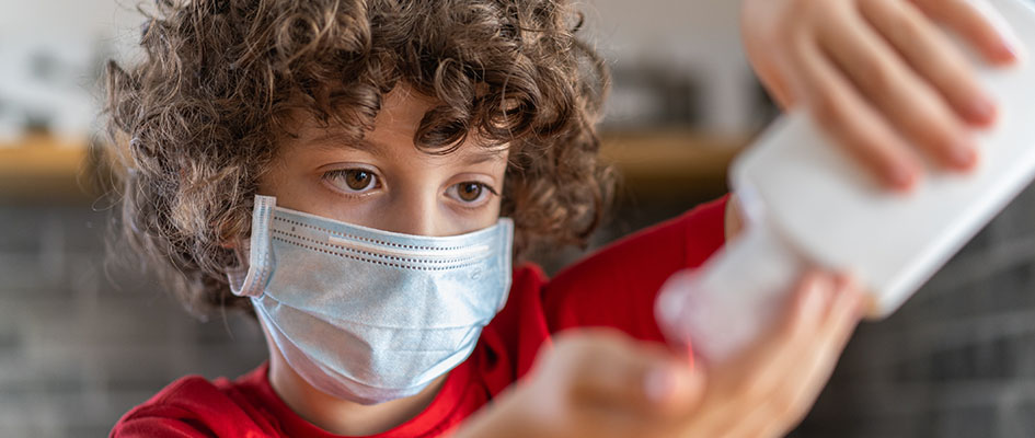 child wearing mask putting on hand sanitiser